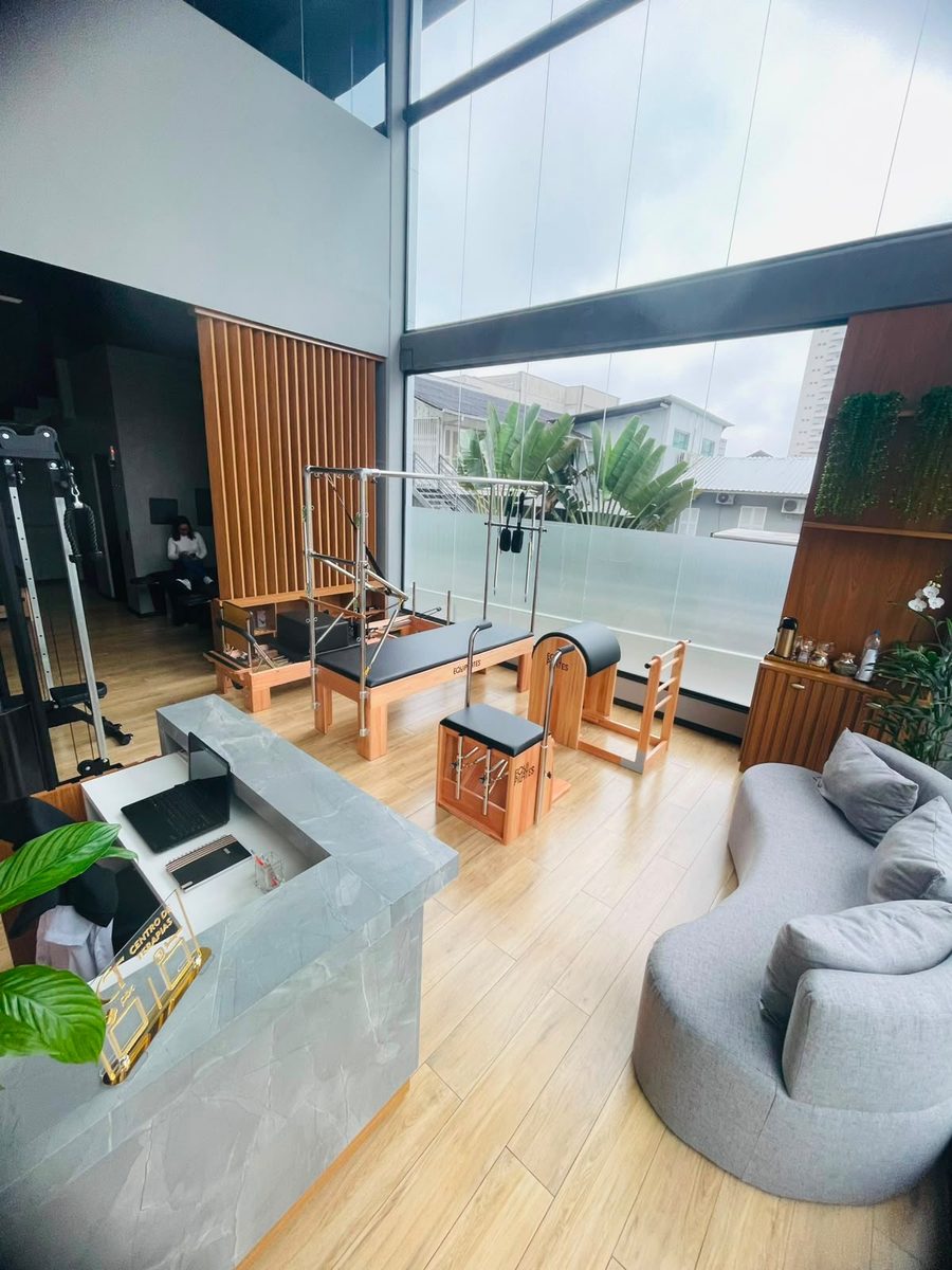 Salão principal do Centro de Terapias, com aparelhos de pilates, janelão de vidro e sofá de espera