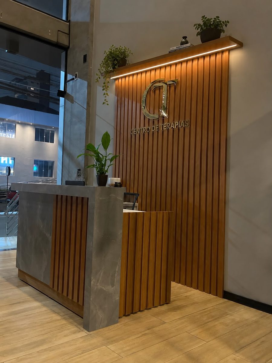 Recepção do Centro de Terapias, com balcão e a logo da clínica em painel ripado de madeira